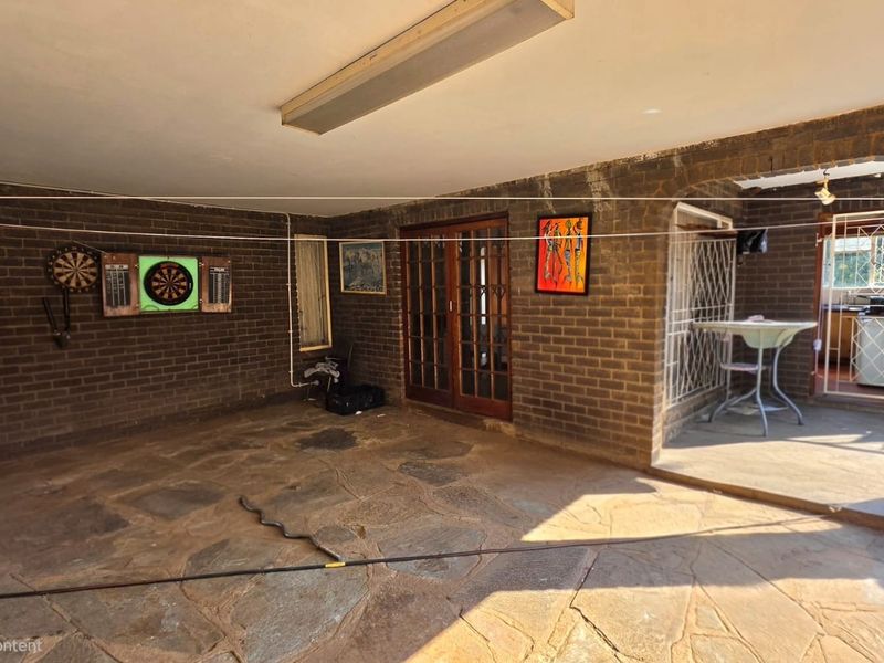 A covered outdoor patio area featuring exposed brick walls, stone flooring, and access to the interior through timber-framed glass doors.