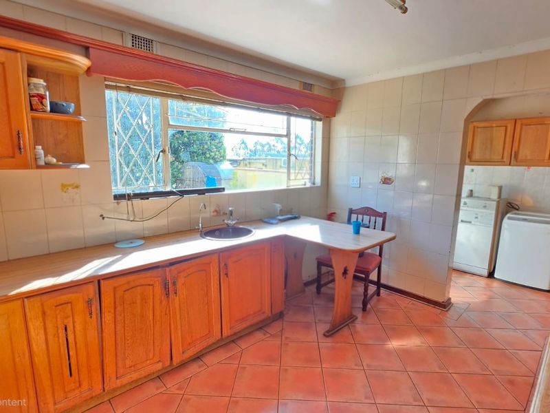 A dated kitchen featuring wooden cabinetry, ceramic wall and floor tiles, and a built-in sink with an adjacent breakfast nook area.
