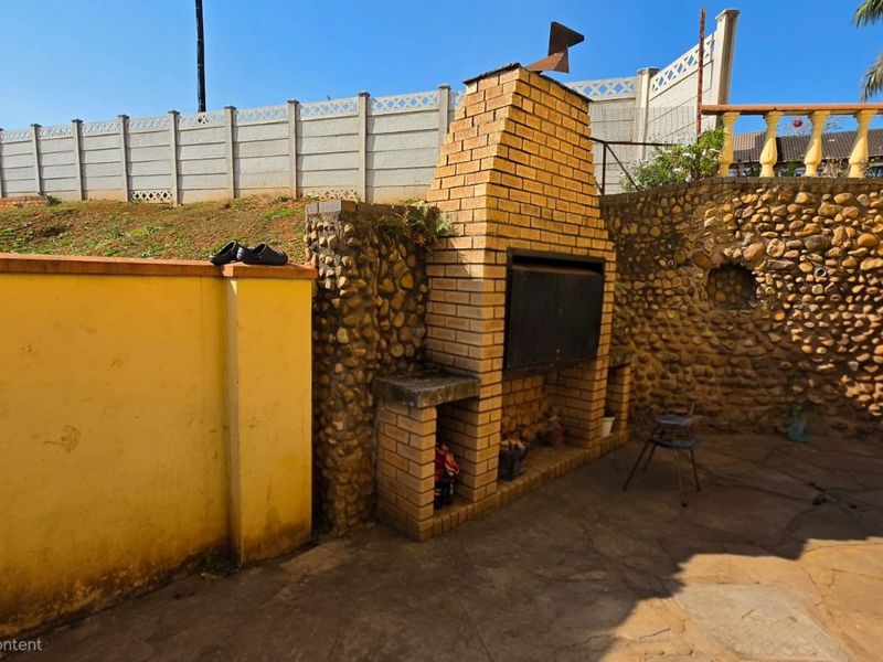 Outdoor patio area featuring a built-in brick braai, stone-clad retaining walls, and paved flooring, providing a functional space for outdoor entertaining.