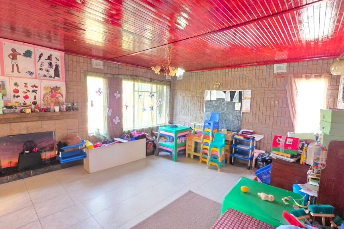 Spacious living area featuring exposed brick walls, tiled flooring, and a distinctive timber ceiling, currently utilized as a play area.
