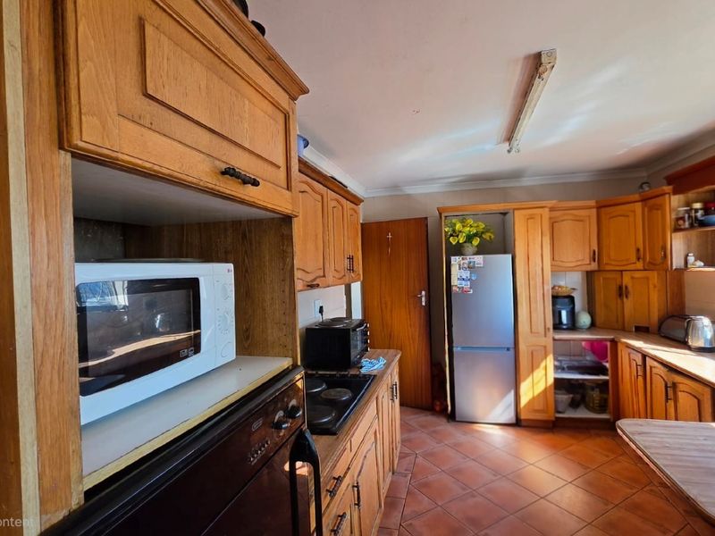 A functional kitchen featuring traditional wooden cabinetry, tiled flooring, and built-in cooking appliances, offering a classic layout with potential for modern updates.