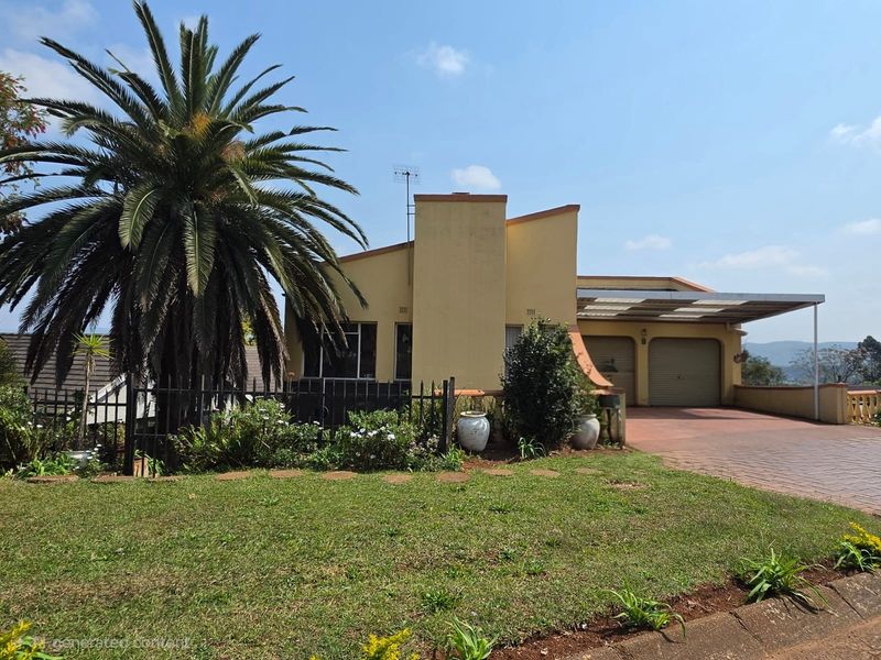 Front elevation of a residential property featuring a double garage, attached carport, paved driveway, and established garden with a prominent palm tree.