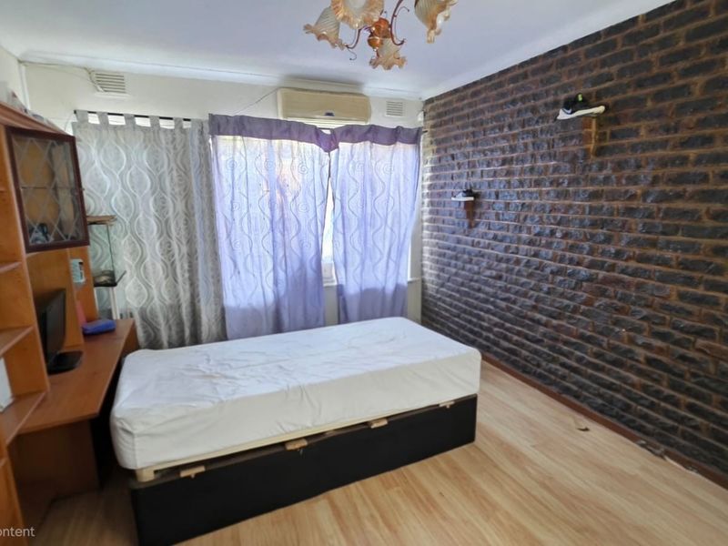 Bedroom featuring an exposed brick feature wall, laminate flooring, and a wall-mounted air conditioning unit.