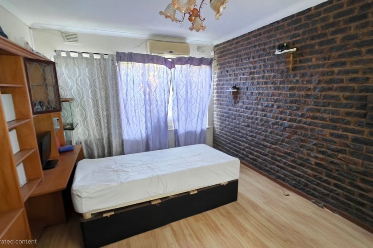 Bedroom featuring an exposed brick feature wall, laminate flooring, and a wall-mounted air conditioning unit.