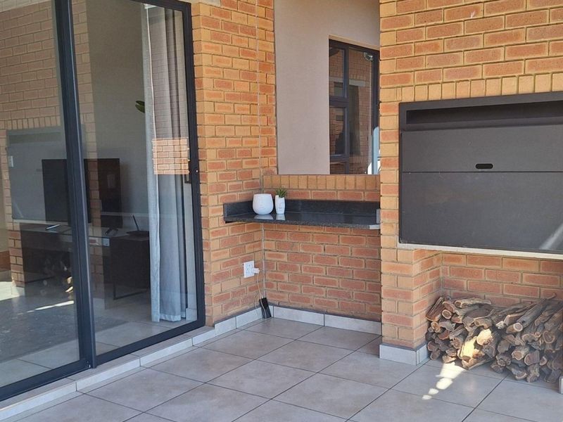 Covered patio area featuring a built-in braai, granite prep counter, and tiled flooring, providing seamless access to the interior living space through sliding doors.
