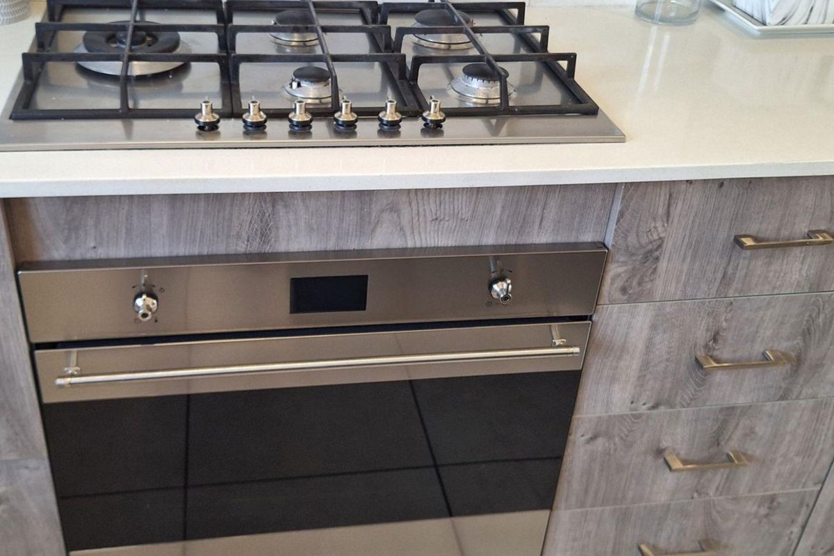 Modern kitchen featuring a stainless steel gas cooktop, built-in oven, and stone countertops with wood-grain laminate cabinetry.