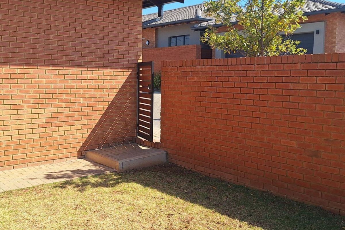 A private rear garden area featuring a brick boundary wall, a secure metal pedestrian gate, and a paved walkway leading to the property.