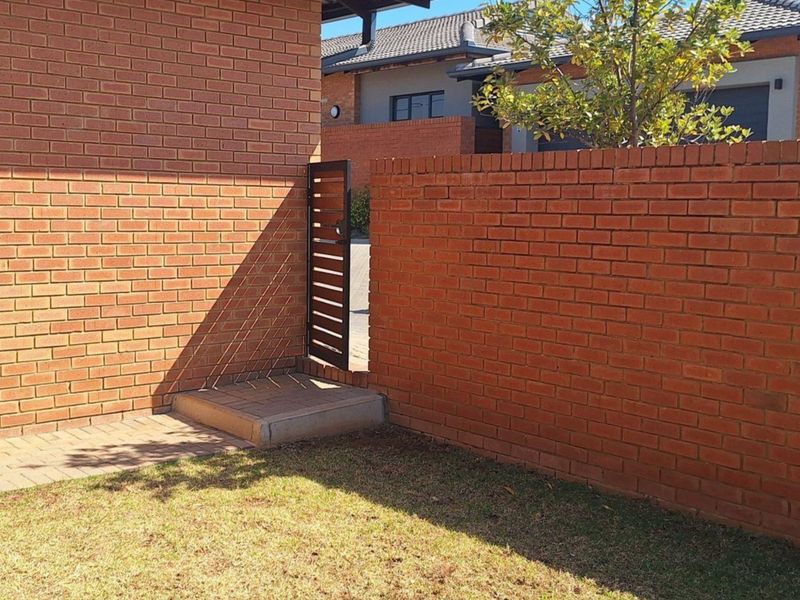 A private rear garden area featuring a brick boundary wall, a secure metal pedestrian gate, and a paved walkway leading to the property.