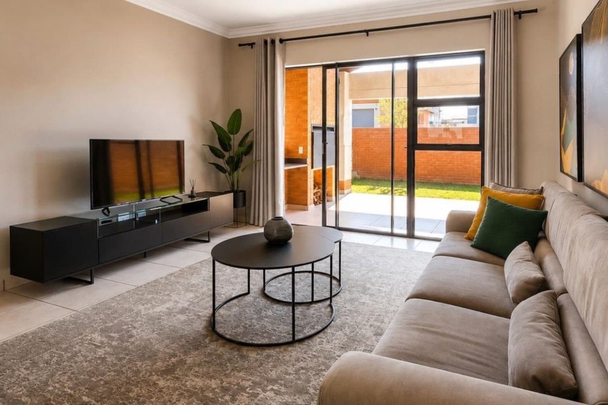 A well-maintained living room featuring tiled flooring and a large sliding glass door that provides seamless access to the outdoor patio area.
