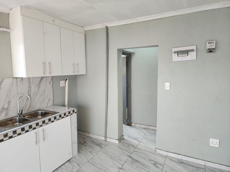 A compact kitchen featuring white cabinetry, marble-look tiled flooring, and a double sink, requiring minor cosmetic updates to improve its overall aesthetic appeal.