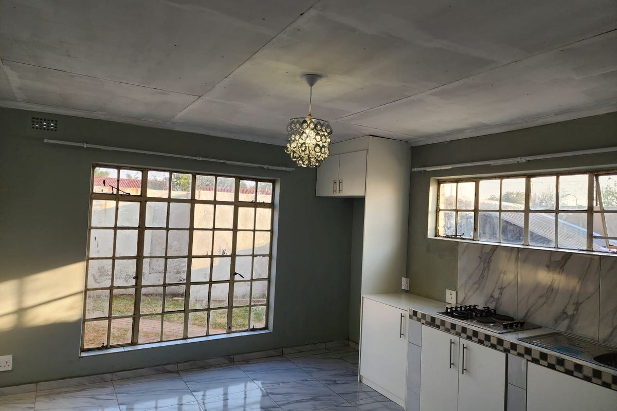 Open-plan kitchen and living area featuring marble-effect tiled floors, built-in cabinetry with gas hob, and large steel-framed windows with garden views.