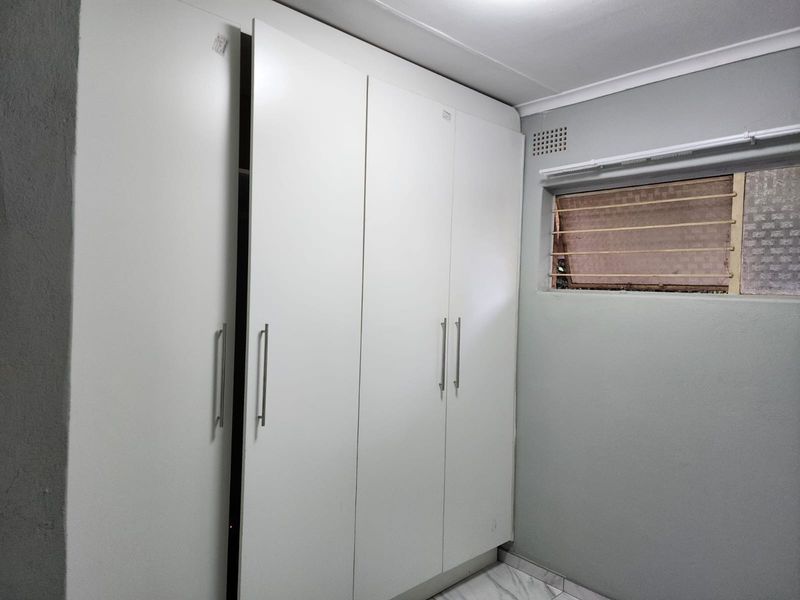 A bedroom featuring built-in white wardrobes, tiled flooring, and a window with security bars.