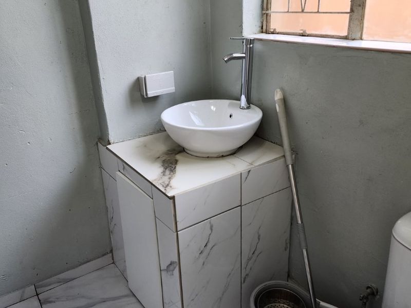 A compact bathroom featuring a modern vessel sink on a marble-look tiled vanity, complemented by matching floor tiles and a standard toilet.