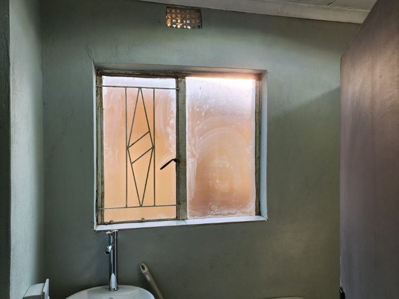 A compact bathroom featuring a vessel sink on a vanity, a standard toilet, and a window with security bars, requiring cosmetic updates.
