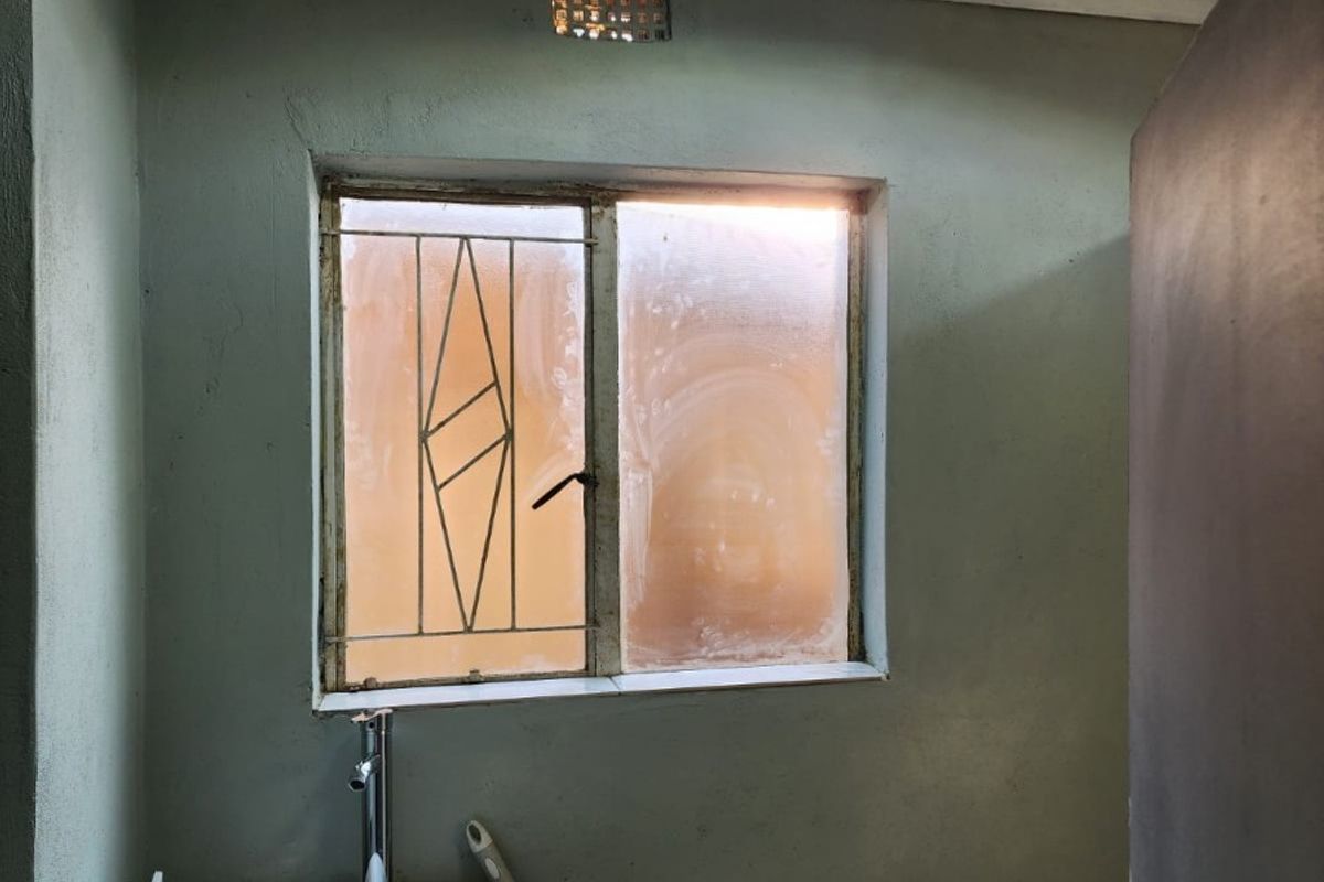 A compact bathroom featuring a vessel sink on a vanity, a standard toilet, and a window with security bars, requiring cosmetic updates.