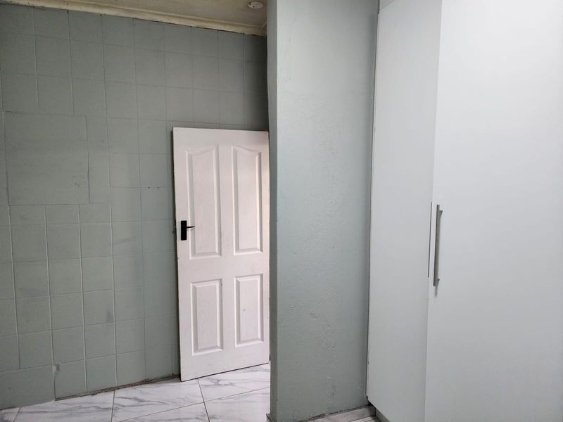 A minimalist bedroom featuring built-in white wardrobes, light grey tiled walls, and marble-effect floor tiles, offering a clean and neutral foundation for interior design.