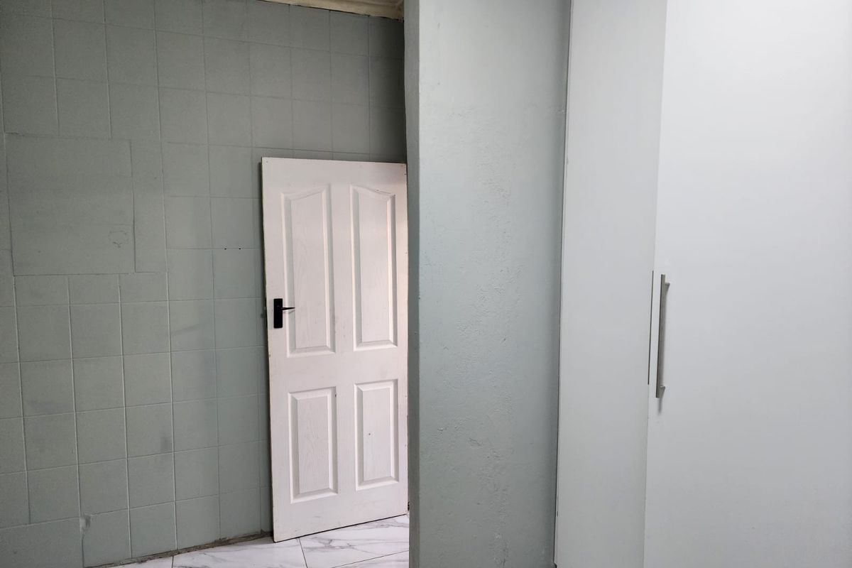 A minimalist bedroom featuring built-in white wardrobes, light grey tiled walls, and marble-effect floor tiles, offering a clean and neutral foundation for interior design.