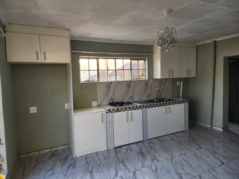 A functional kitchen space featuring built-in cabinetry, a gas hob, stainless steel sink, and marble-look tiled flooring throughout.