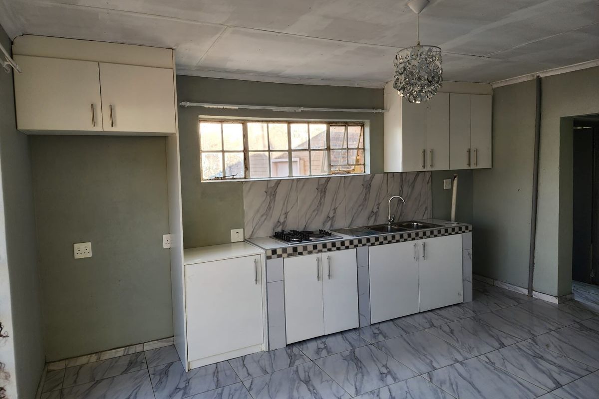 A functional kitchen space featuring built-in cabinetry, a gas hob, stainless steel sink, and marble-look tiled flooring throughout.