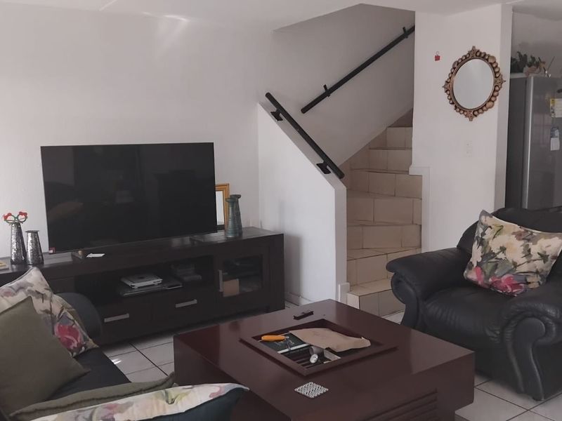Open plan living area featuring tiled flooring and a staircase with a metal handrail, providing a functional layout for the townhouse.