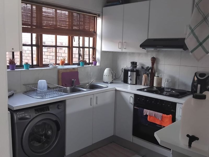 Compact kitchen featuring white cabinetry, tiled backsplash, built-in oven with hob, extractor fan, and integrated laundry appliance space.