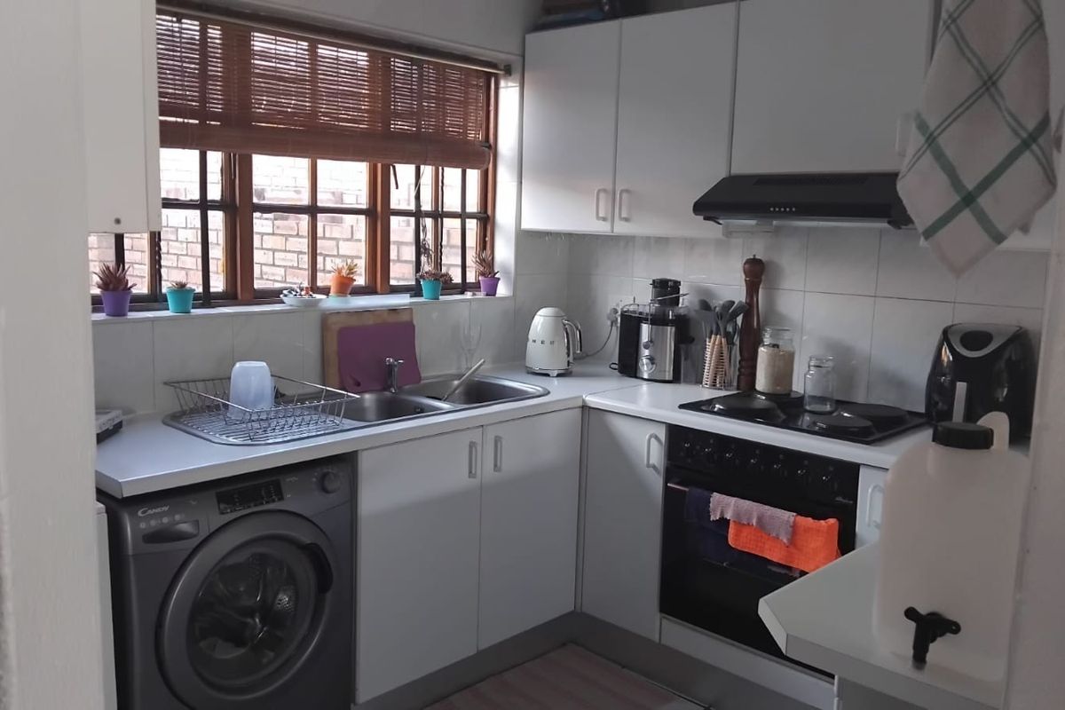Compact kitchen featuring white cabinetry, tiled backsplash, built-in oven with hob, extractor fan, and integrated laundry appliance space.