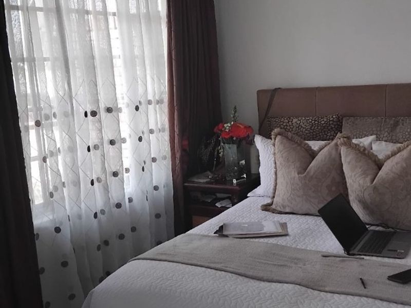A cozy bedroom featuring tiled flooring and large windows with curtain treatments, providing natural light to the space.