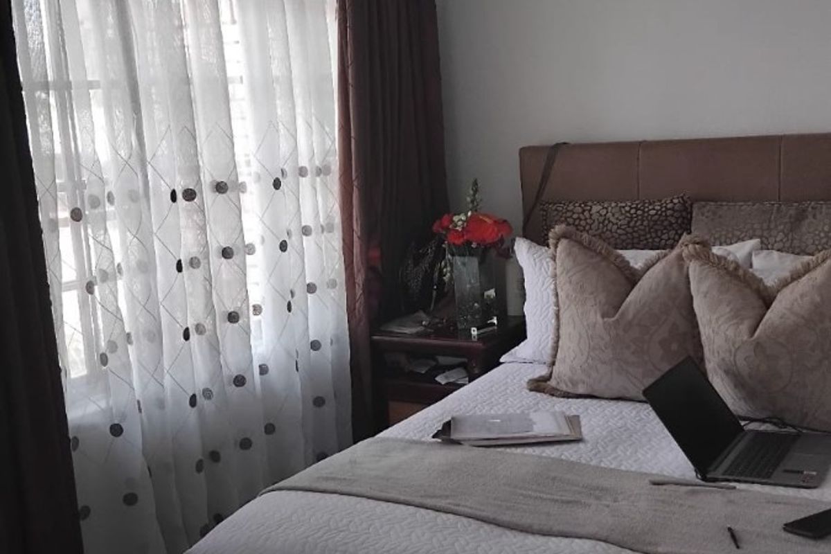 A cozy bedroom featuring tiled flooring and large windows with curtain treatments, providing natural light to the space.