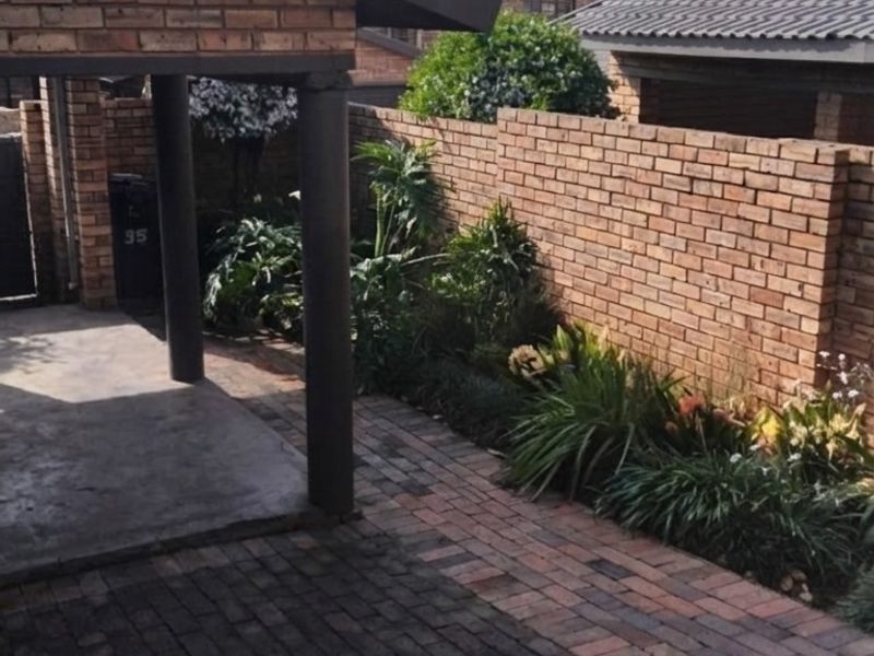 A private rear courtyard featuring a covered patio area, brick boundary walls, and neatly paved flooring with established garden beds.