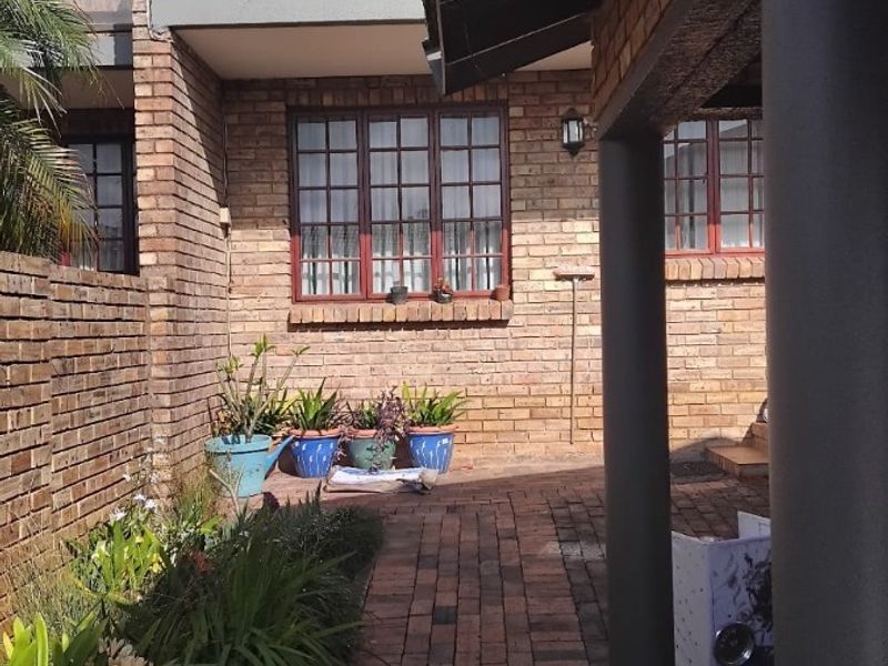 A rear exterior view of a townhouse featuring a brick facade, a paved patio area, and an upper-level balcony.