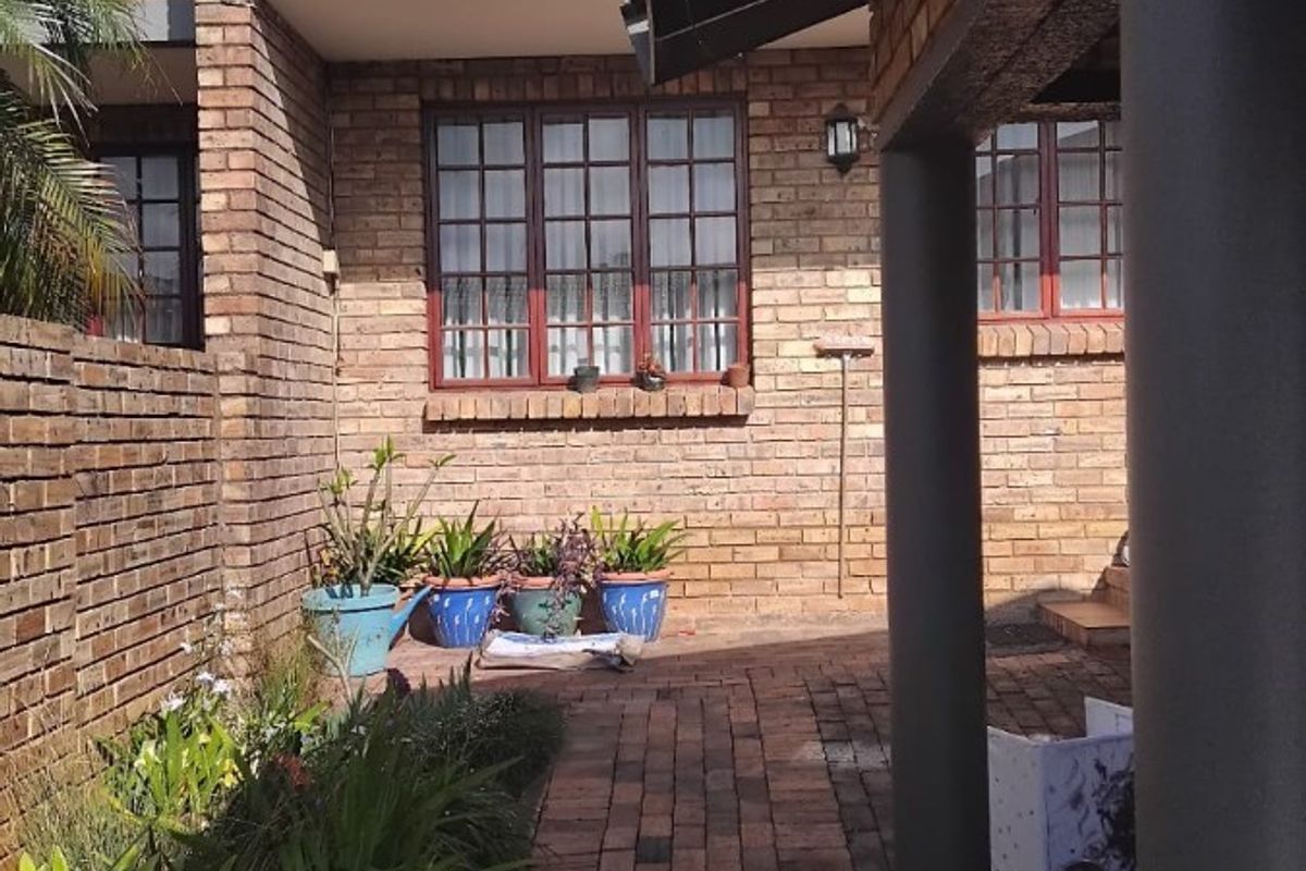A rear exterior view of a townhouse featuring a brick facade, a paved patio area, and an upper-level balcony.