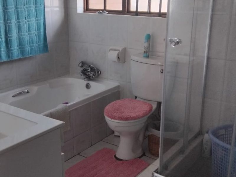 A functional bathroom featuring a built-in bathtub, separate glass shower enclosure, toilet, and vanity cabinet with tiled finishes throughout.