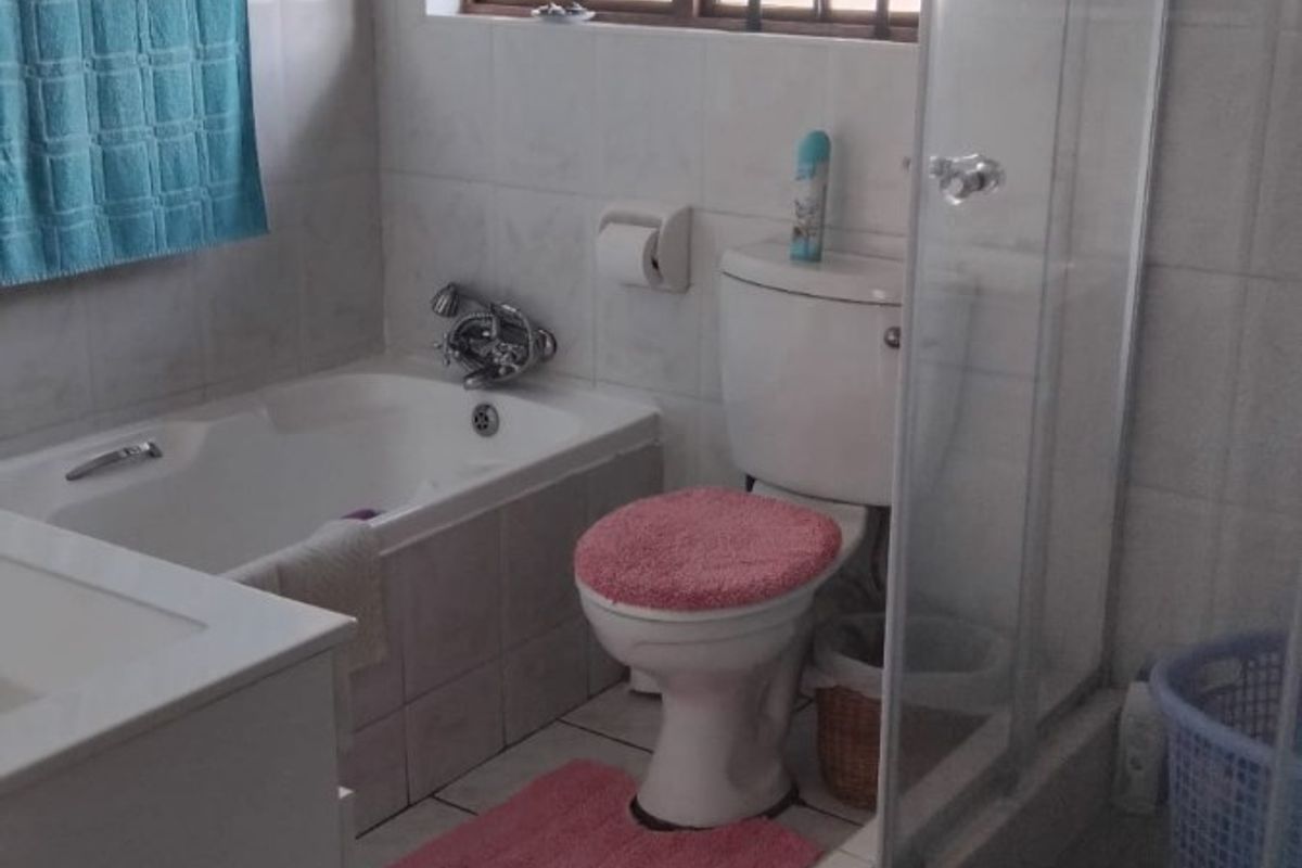 A functional bathroom featuring a built-in bathtub, separate glass shower enclosure, toilet, and vanity cabinet with tiled finishes throughout.