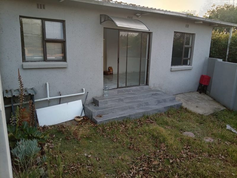 Rear exterior view of the property featuring a sliding glass door, tiled entrance steps, and an awning, with an adjacent garden area.