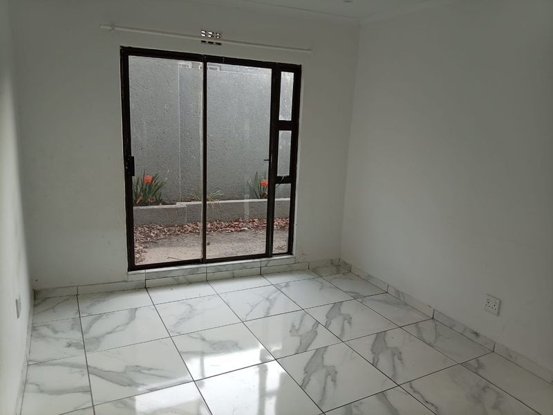 An empty bedroom featuring modern marble-look floor tiles and a sliding glass door providing access to a small private courtyard area.