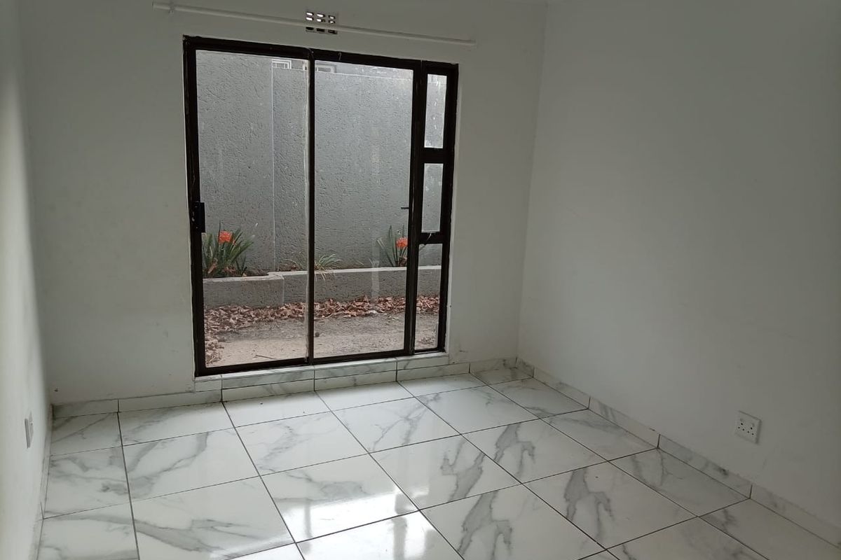 An empty bedroom featuring modern marble-look floor tiles and a sliding glass door providing access to a small private courtyard area.