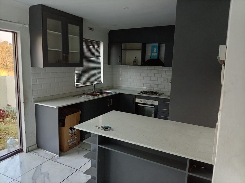 Modern kitchen featuring dark cabinetry, stone countertops, subway tile backsplash, integrated gas hob, oven, and a functional breakfast bar area.