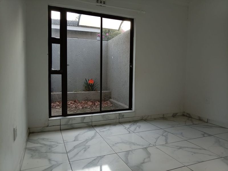 An empty bedroom featuring modern marble-look floor tiles and a large sliding glass door providing access to a private courtyard area.