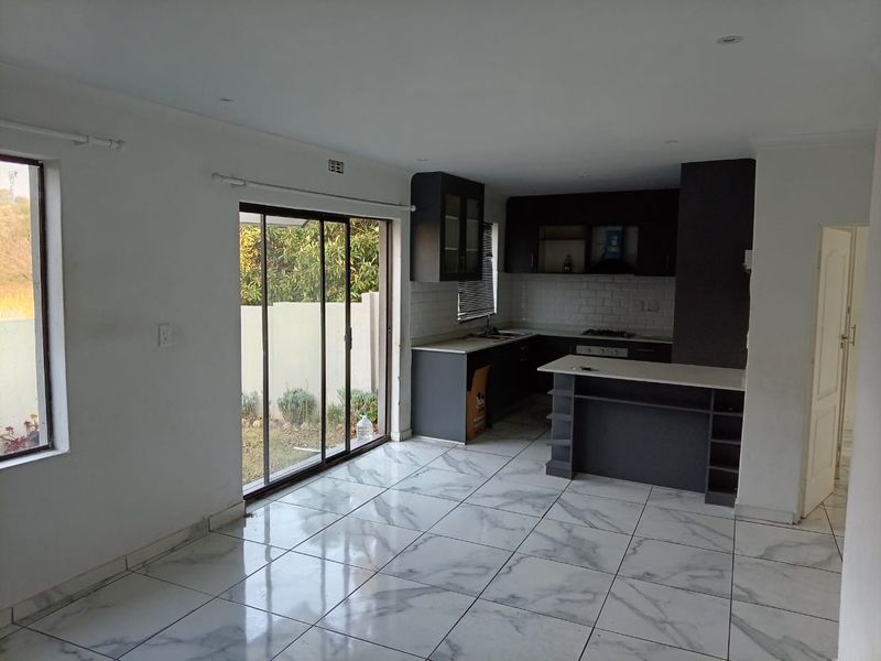 Modern open-plan living and kitchen area featuring marble-look floor tiles, sleek dark cabinetry, a kitchen island, and sliding glass doors leading to the garden.