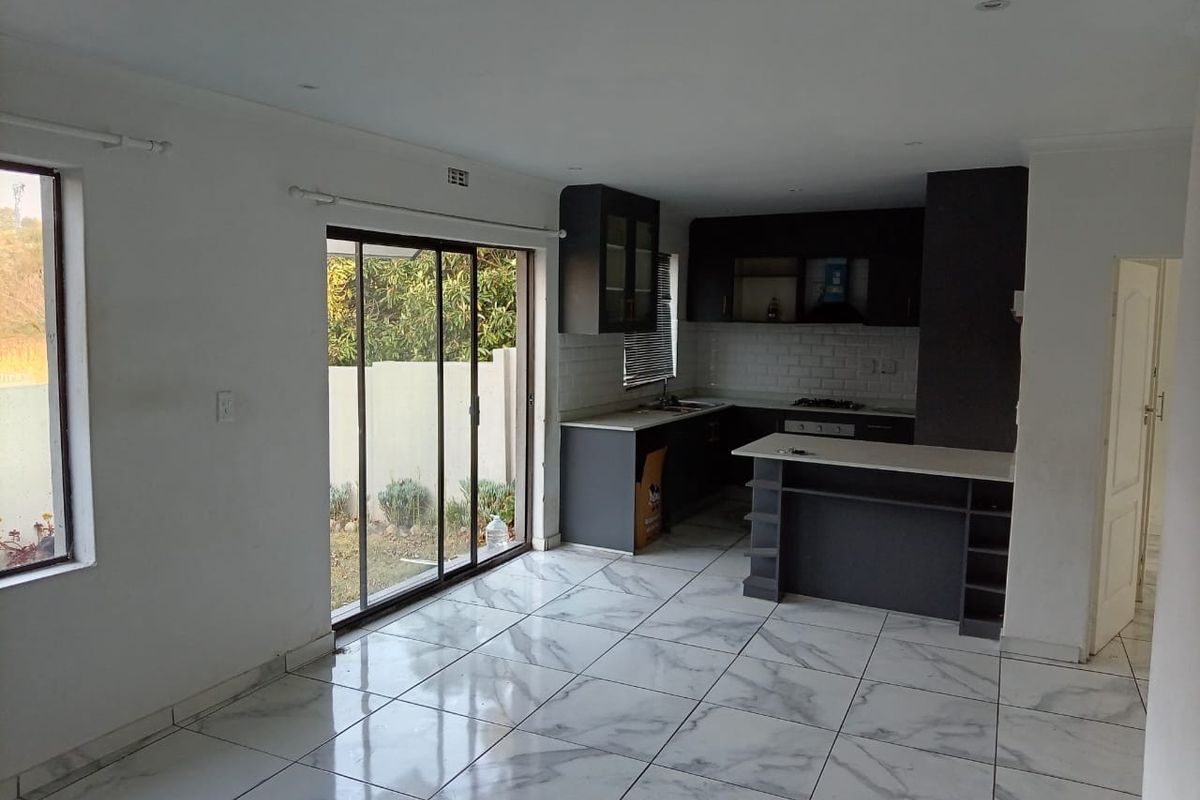Modern open-plan living and kitchen area featuring marble-look floor tiles, sleek dark cabinetry, a kitchen island, and sliding glass doors leading to the garden.