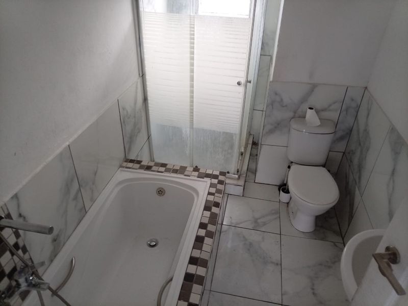 A compact bathroom featuring a built-in bathtub, separate shower enclosure, toilet, and bidet with marble-effect tiling throughout.