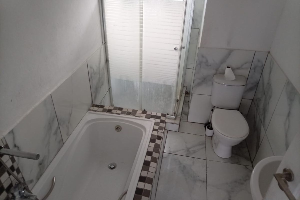 A compact bathroom featuring a built-in bathtub, separate shower enclosure, toilet, and bidet with marble-effect tiling throughout.