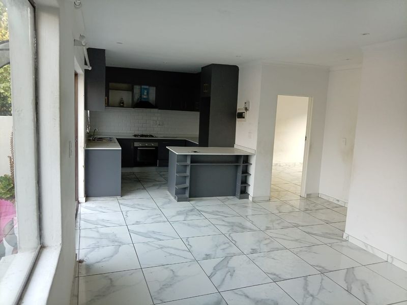 Open-plan kitchen and living area featuring modern dark cabinetry, built-in appliances, and marble-look floor tiles, offering a clean and functional space.