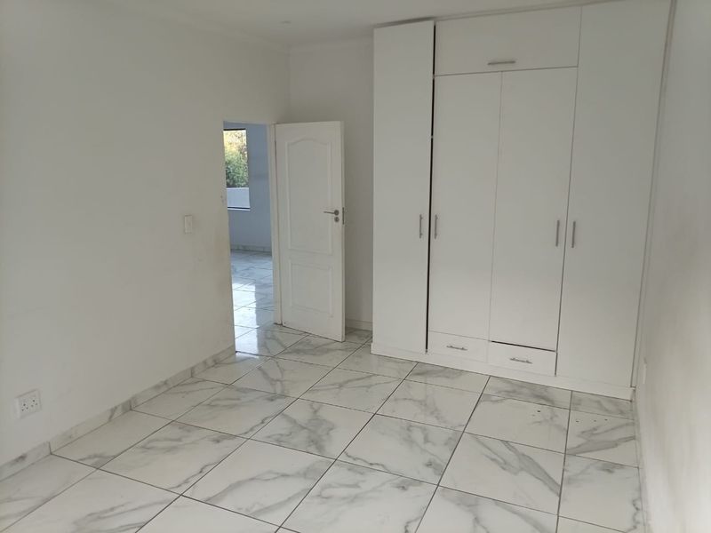 A bright, empty bedroom featuring modern marble-look floor tiles and a large white built-in wardrobe.