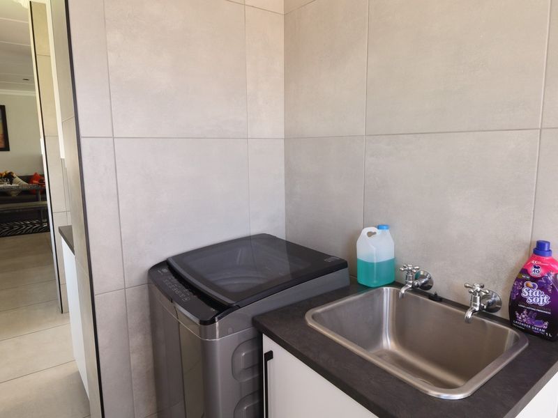 A functional laundry area featuring a stainless steel sink, tiled walls, and built-in cabinetry with a laminate countertop.