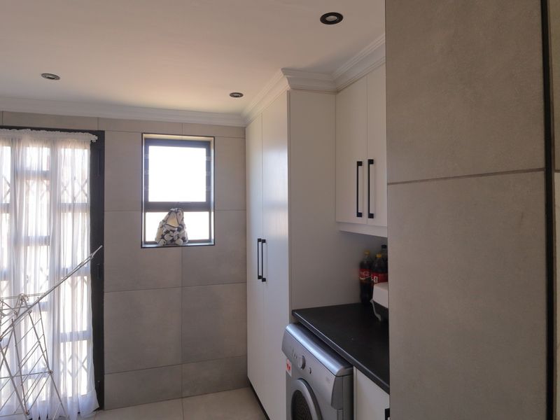 A functional laundry room featuring modern grey wall tiles, built-in cabinetry with dark countertops, and direct access to an outdoor area via a security door.