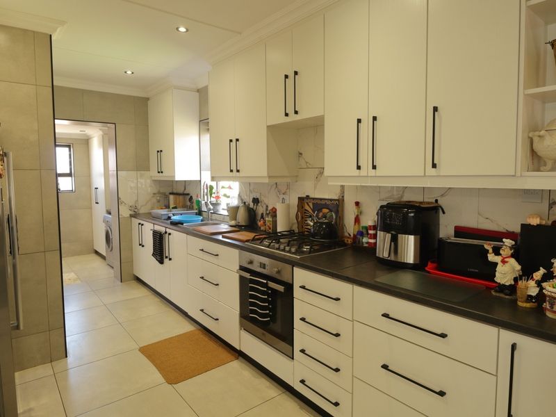 Modern kitchen featuring white cabinetry, dark stone countertops, gas hob, built-in oven, and marble-look backsplash with tiled flooring.