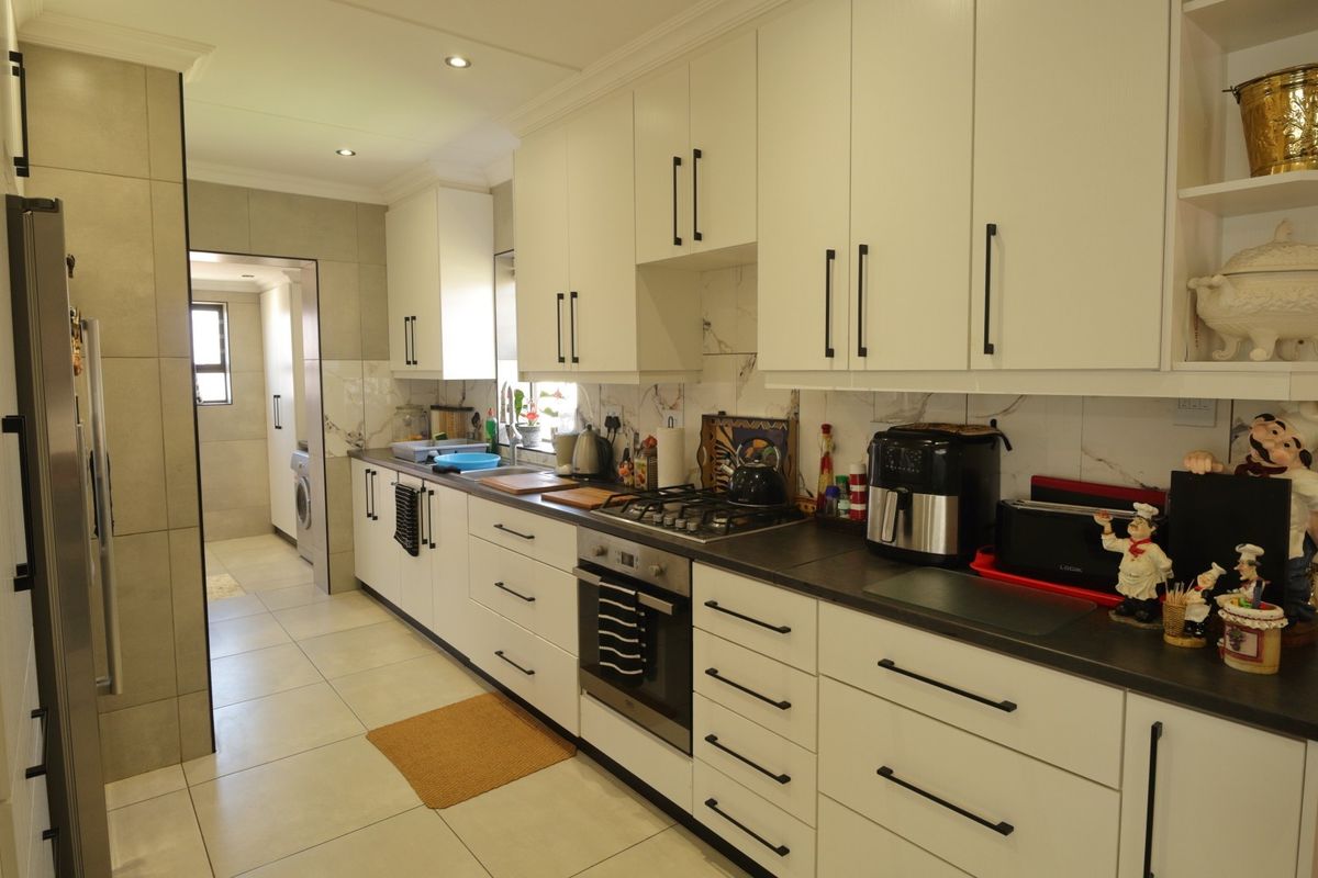 Modern kitchen featuring white cabinetry, dark stone countertops, gas hob, built-in oven, and marble-look backsplash with tiled flooring.