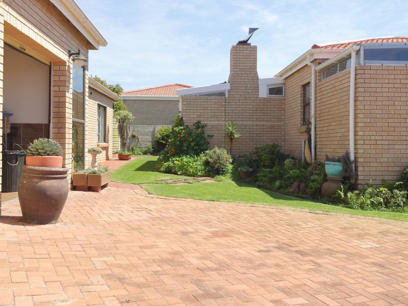 A well-maintained rear courtyard featuring brick paving, a landscaped lawn, and face brick exterior walls with a prominent chimney.
