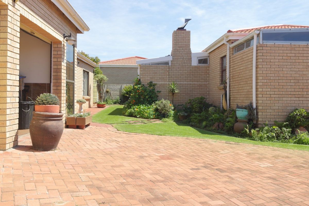 A well-maintained rear courtyard featuring brick paving, a landscaped lawn, and face brick exterior walls with a prominent chimney.